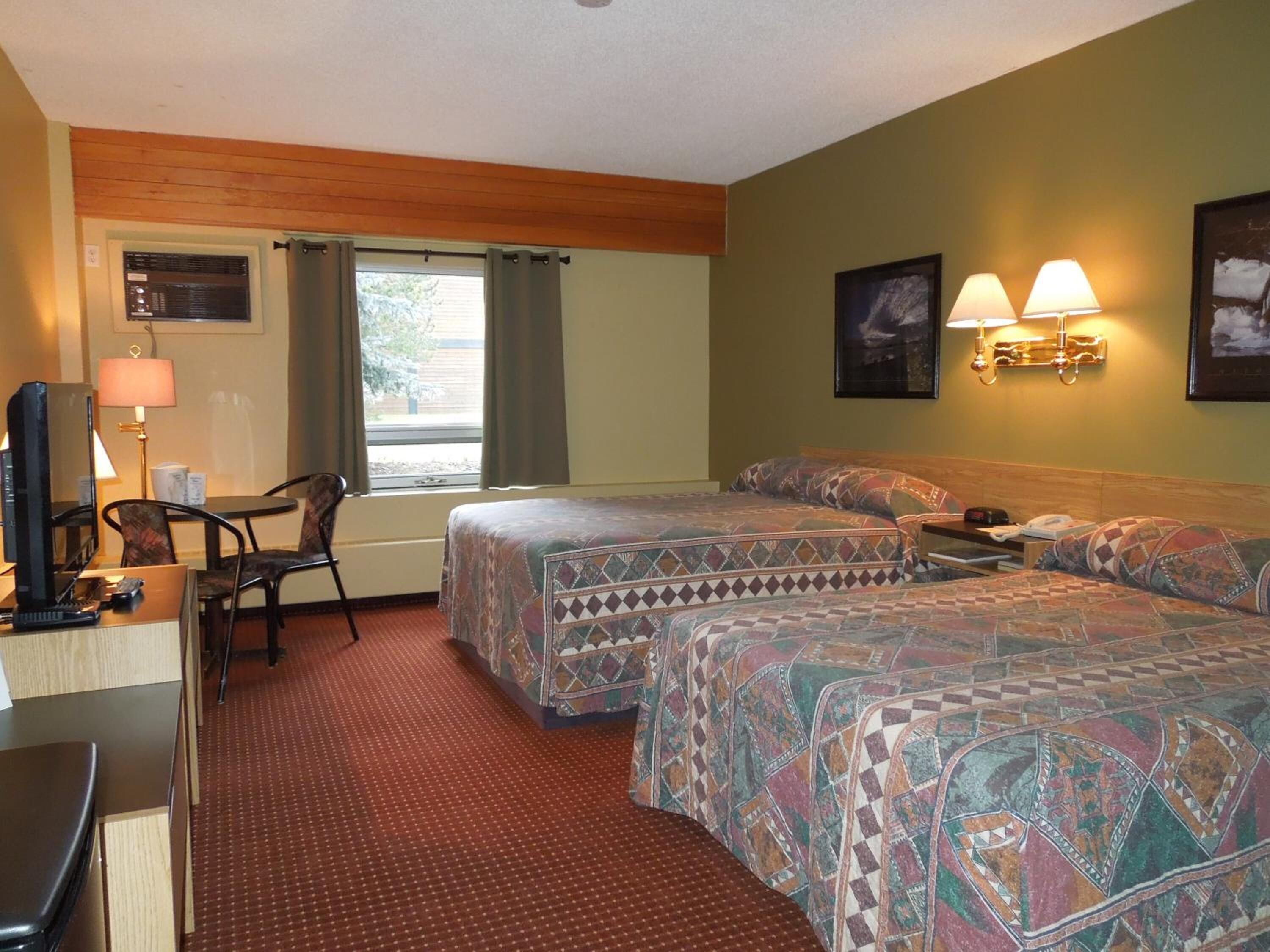 A hotel room with two beds, a desk with a computer, a chair, and a window with curtains.