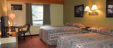 A hotel room with two beds, a desk with a computer, a chair, and a window with curtains.