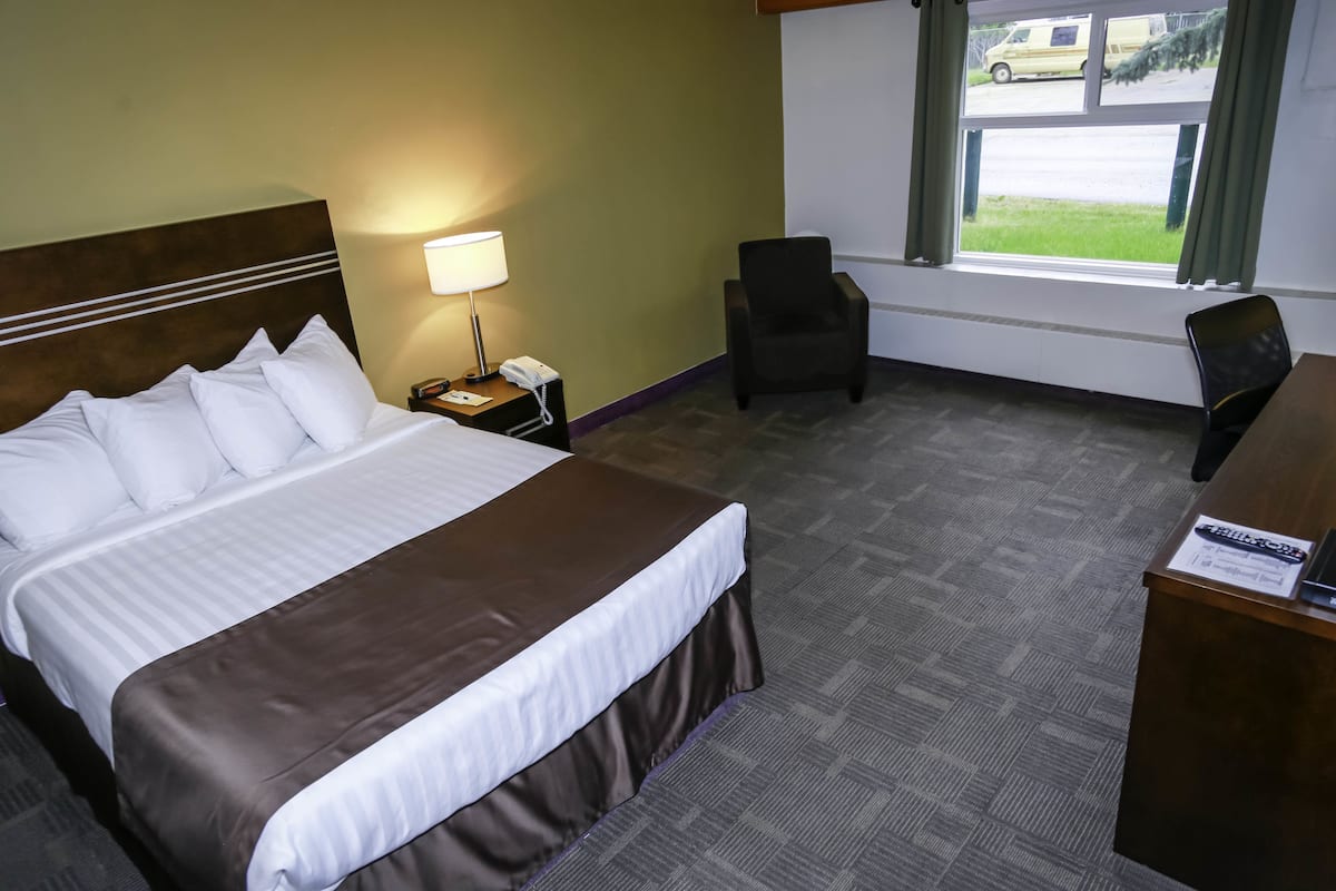 A hotel room with a large bed, a desk, a chair, a lamp, and a window with a view of a parking lot.