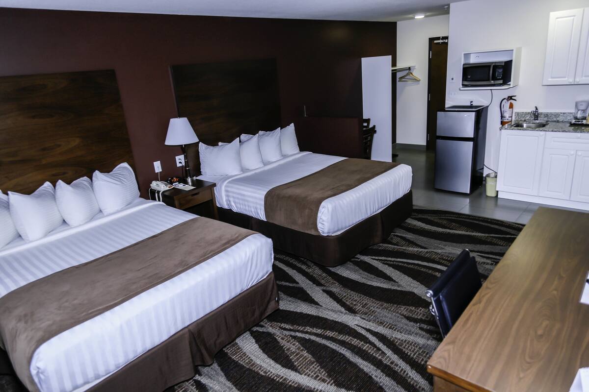 A hotel room with two beds, a desk, a microwave, and a refrigerator.