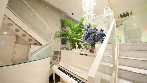 Un pianoforte a coda in un'ampia sala, elegantemente arredata con una scala e un lampadario.