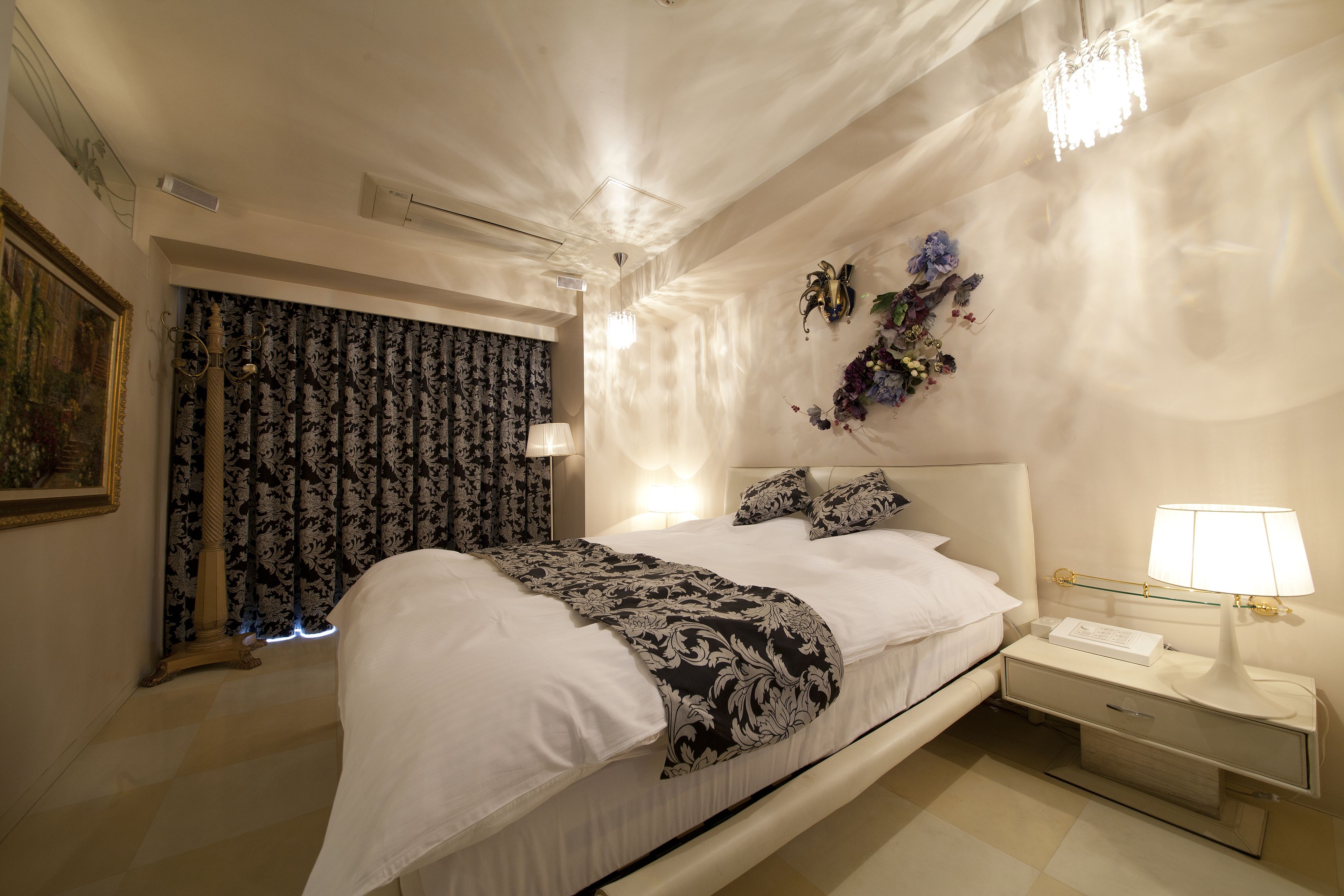 Una cama bien hecha con una manta estampada, una mesita de noche con lámpara y un adorno de pared.