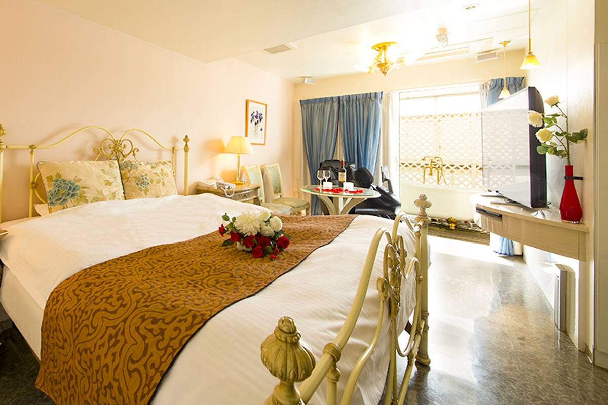 A hotel room with a bed, bedside tables, a desk, a chair, and a mirror.