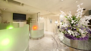 Una hall d'hotel moderna con una reception, una televisione, un divisorio in vetro e un composito floreale.