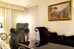 Una habitación con una silla reclinable negra, una silla blanca y un cuadro en la pared.