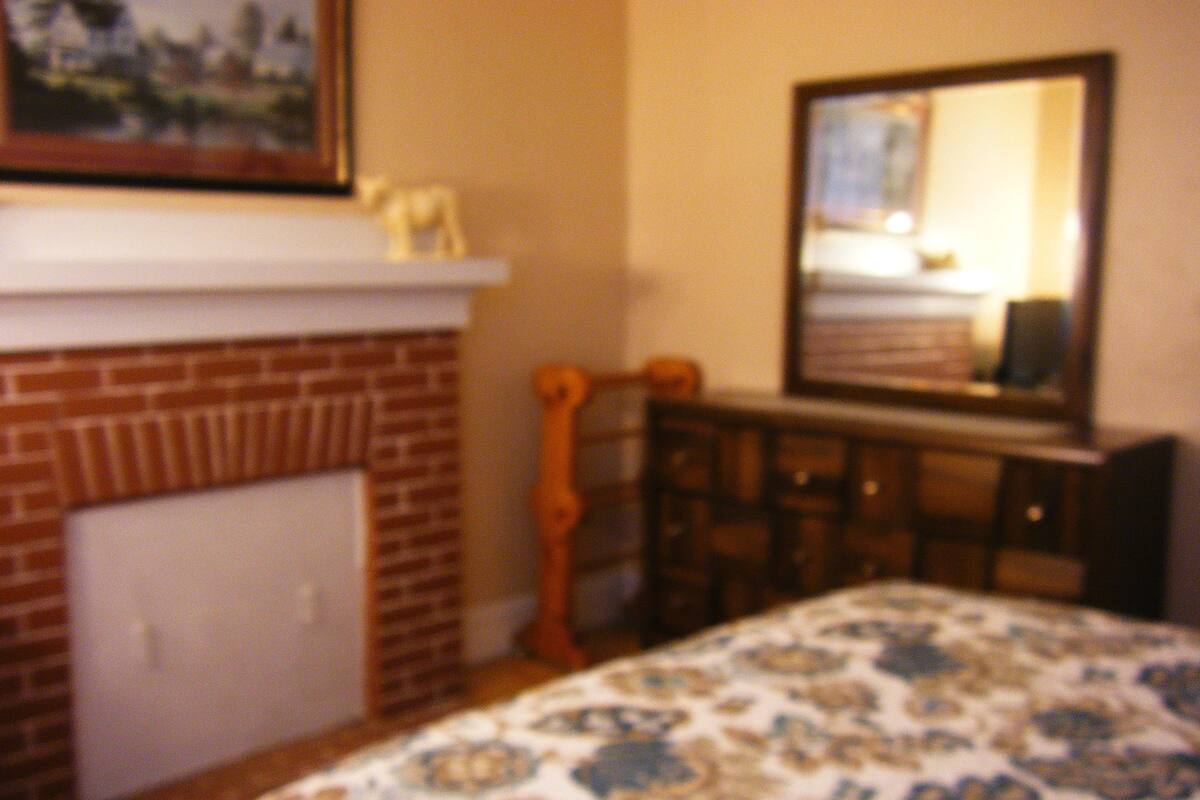 A bedroom with a brick fireplace, a wooden dresser, and a bed with a patterned bedspread.