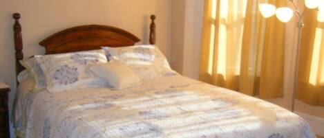 A neatly made bed with a floral-patterned bedspread and pillows, a wooden headboard, and a nightstand with a lamp.