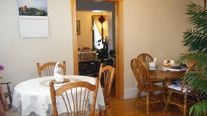 A dining area with wooden chairs and a round table, a calendar on the wall, and a plant in the corner. - Glory Guest House (Moncton)