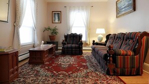 A living room with a patterned rug, a striped armchair, a sofa, and a side table with a lamp. - Glory Guest House (Moncton)