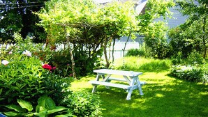 A garden with a white picnic table surrounded by lush greenery and flowering plants. - Glory Guest House (Moncton)