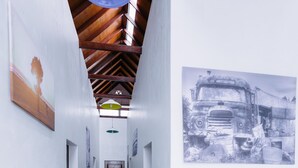 A hallway with wooden floors, white walls, and a ceiling fan. There are framed pictures on the walls and a door at the end. - Westwood Highland - Hostel (Kampung Raja)