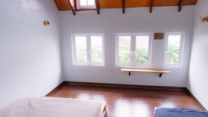 A room with two beds, wooden flooring, a sloped ceiling, and windows with views of greenery. - Westwood Highland - Hostel (Kampung Raja)