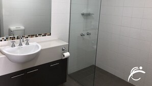 A modern bathroom with a glass shower enclosure, a white sink with a mirror, and a toilet paper holder. - Coro Club Motel (Griffith)