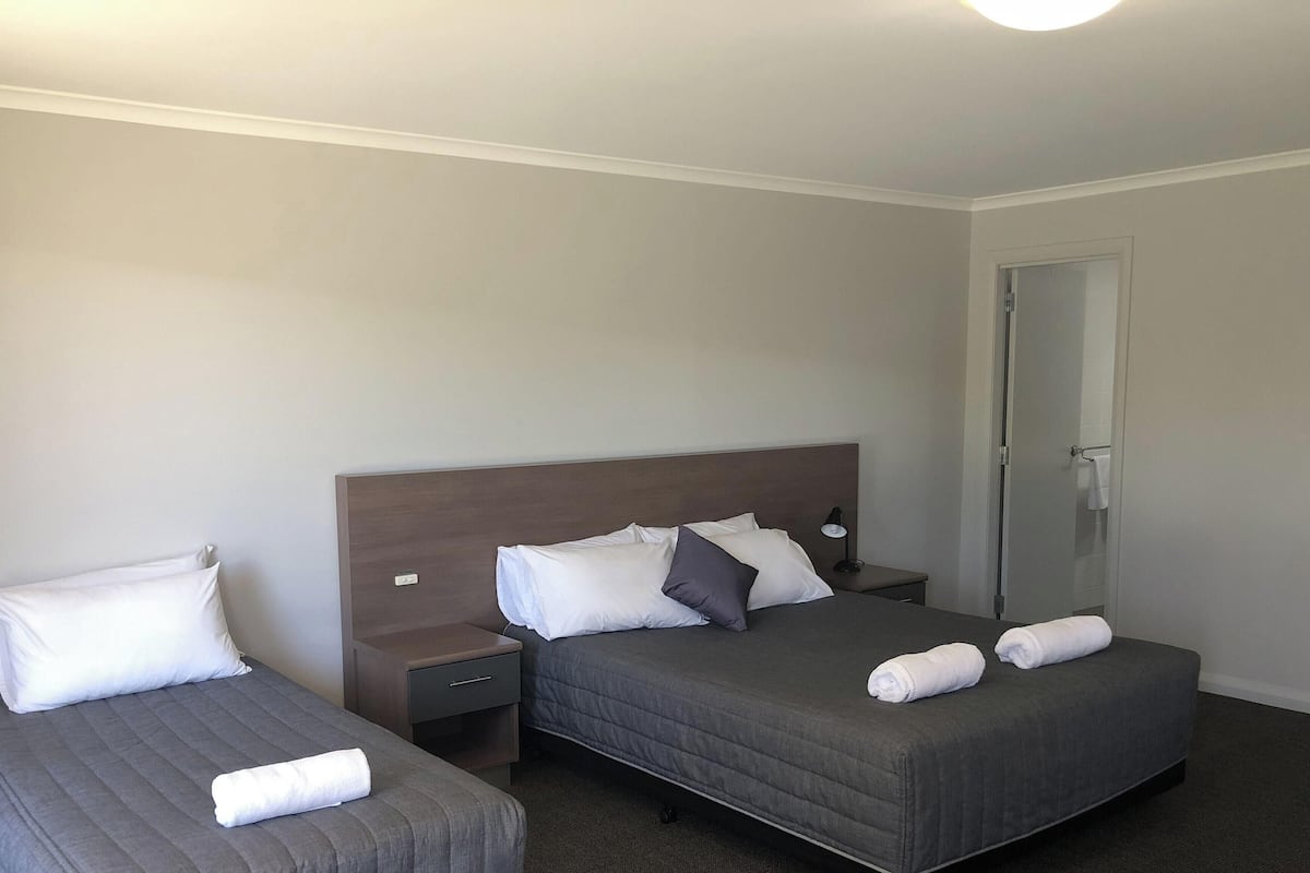 A hotel room with two single beds, a nightstand with a lamp, and a door.