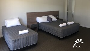 A hotel room with two single beds, a nightstand with a lamp, and a door leading to a bathroom. - Coro Club Motel (Griffith)