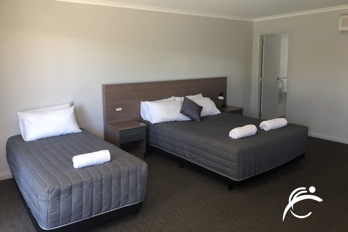 A hotel room with two single beds, a nightstand with a lamp, and a door leading to a bathroom.