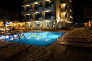 A swimming pool with lounge chairs and a building with multiple balconies in the background. - Bora Bora (Nessebar)