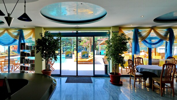 Vestíbulo de hotel con mostrador de recepción, zona de estar y plantas en macetas.