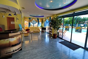 A hotel lobby with a reception desk, seating area, and a view of the outdoor pool area. - Bora Bora (Nessebar)