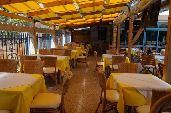 An indoor dining area with tables and chairs, a tiled floor, and a wooden ceiling structure. - Bora Bora (Nessebar)
