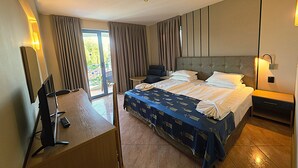 Habitación de hotel con cama, escritorio con silla, una mesita y balcón con cortinas.