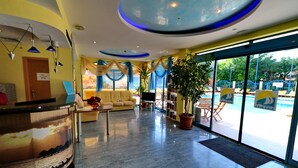 Un vestíbulo de hotel con mostrador de recepción, zona de estar y vista a la piscina.