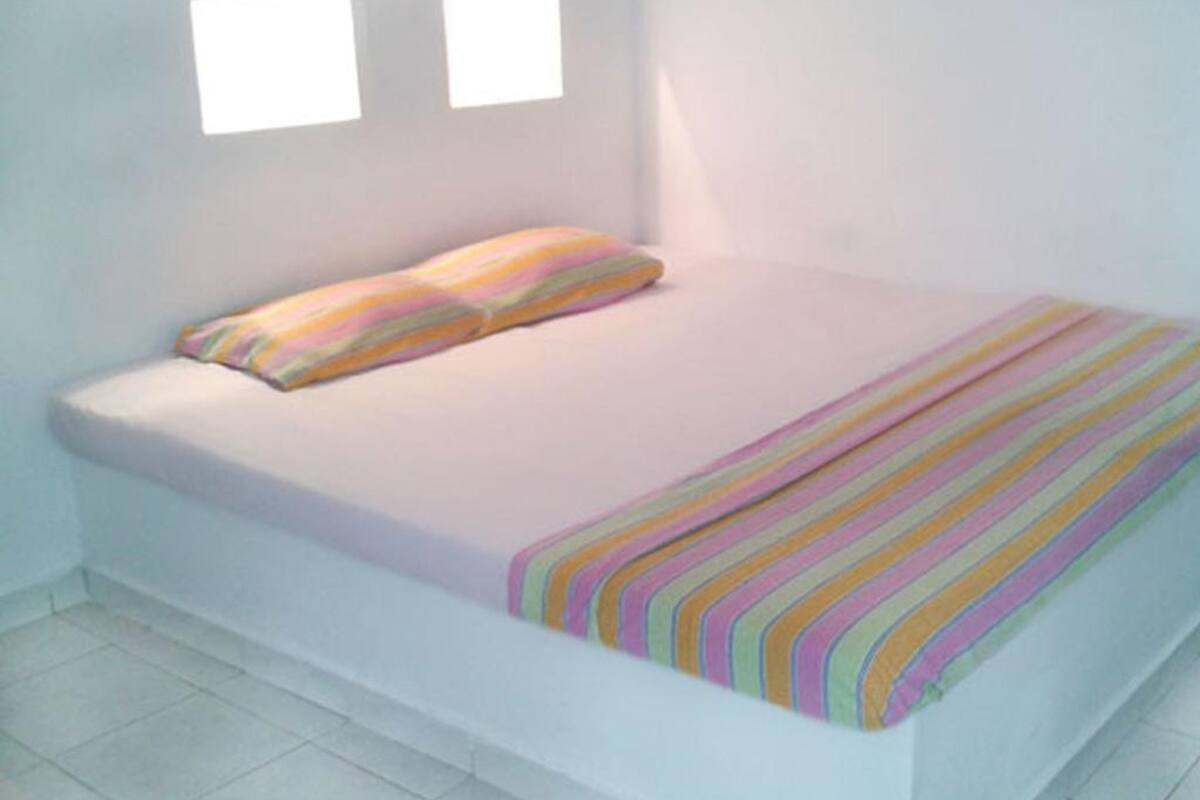 A single bed with a striped blanket and two pillows in a room with white walls and a tiled floor.