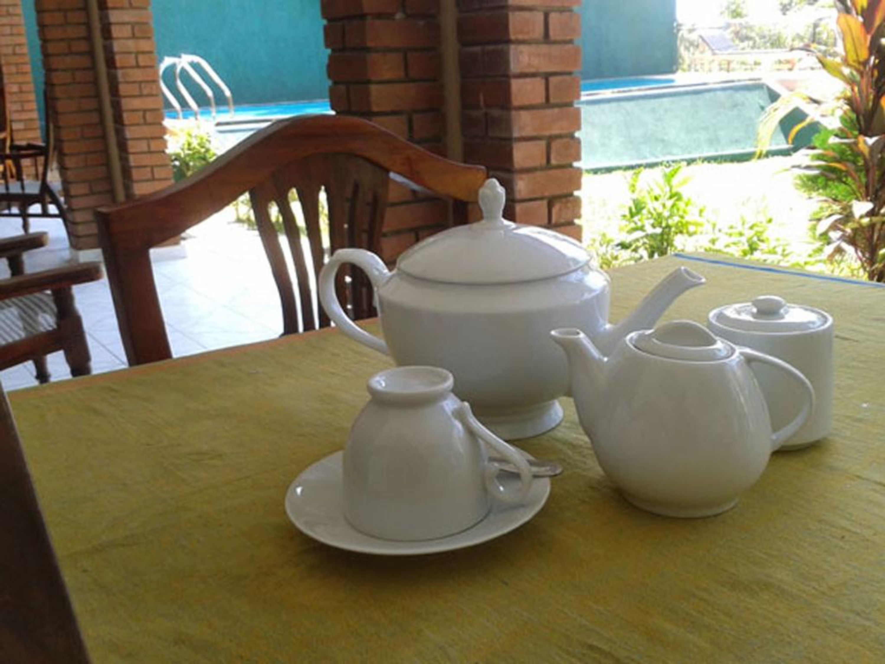 A table with a tea set including a teapot, a cup, and a saucer, set against a yellow tablecloth.