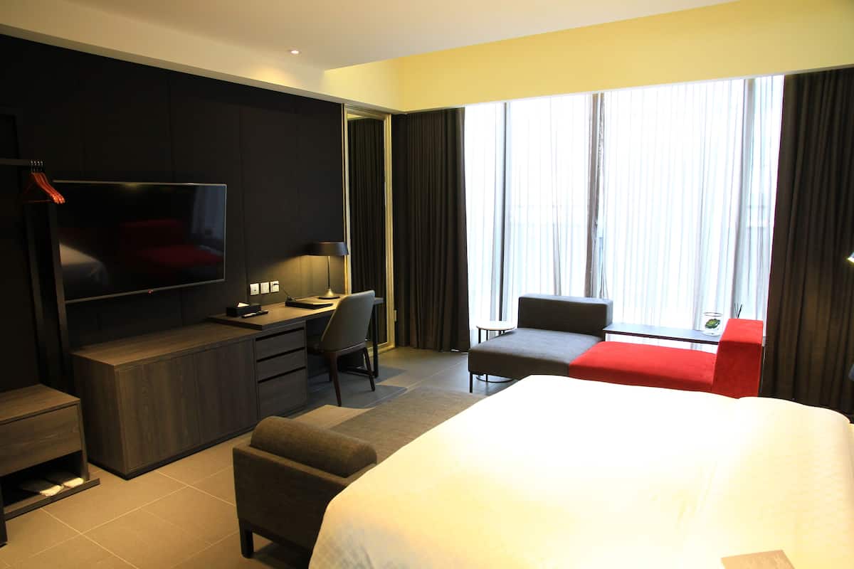 Ein Hotelzimmer mit einem großen Bett, einem Schreibtisch mit Stuhl, einem Fernseher und einem Fenster mit Vorhängen.