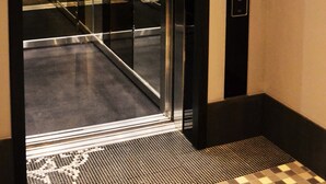 Un ascensore con porta in vetro, pannello di controllo e pulsante di emergenza.