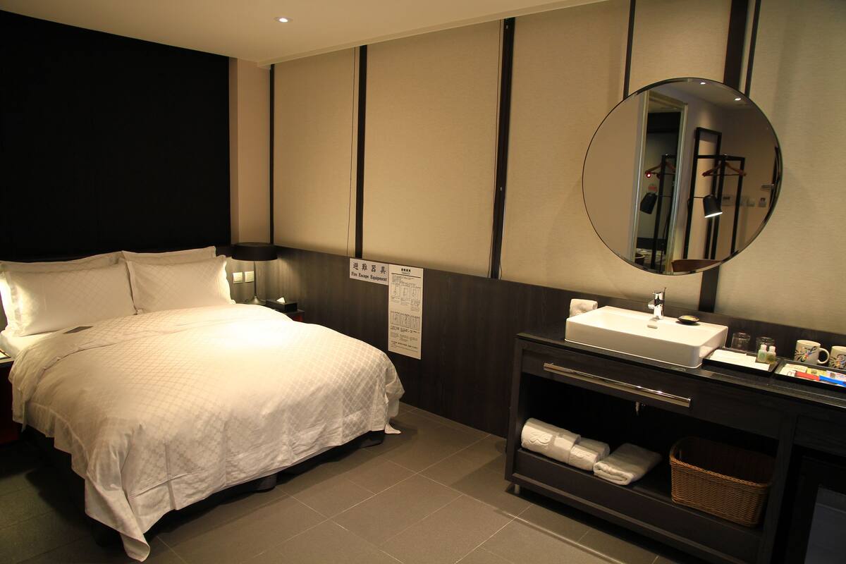 Ein Hotelzimmer mit einem Bett, einem runden Spiegel, einem Waschbecken und einem Regal mit Handtüchern.