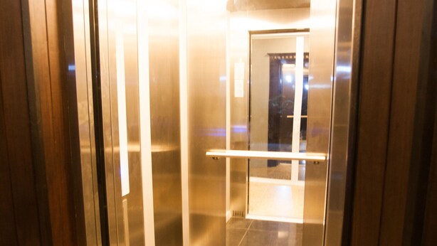 An elevator interior with metallic walls and a reflective floor.