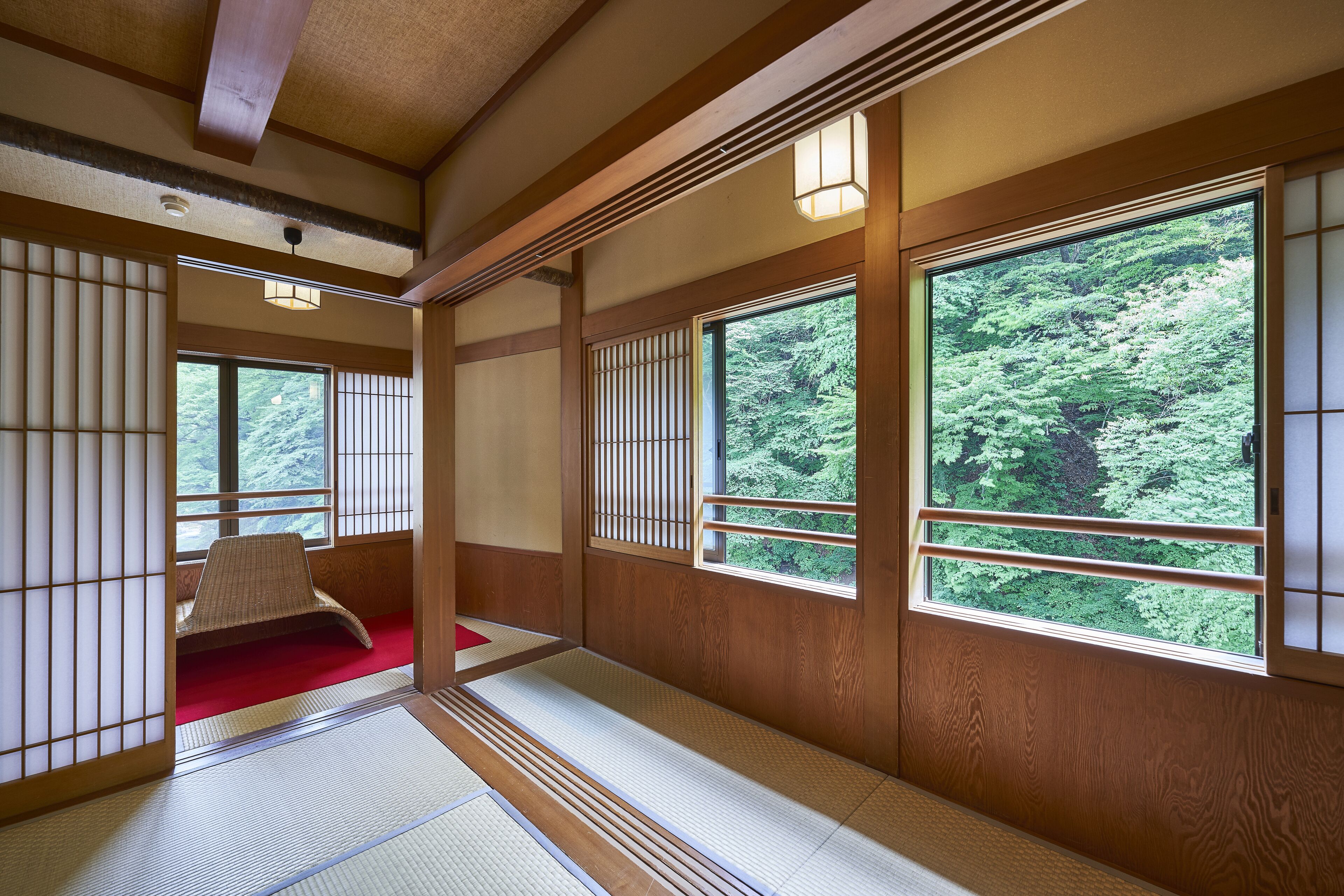 Una habitación japonesa tradicional con suelo de tatami, puertas correderas shoji y grandes ventanales que ofrecen vistas de vegetación exuberante.