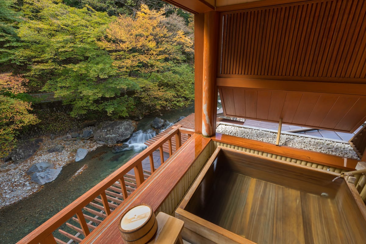 A traditional Japanese onsen with a wooden deck overlooking a natural hot spring surrounded by trees.