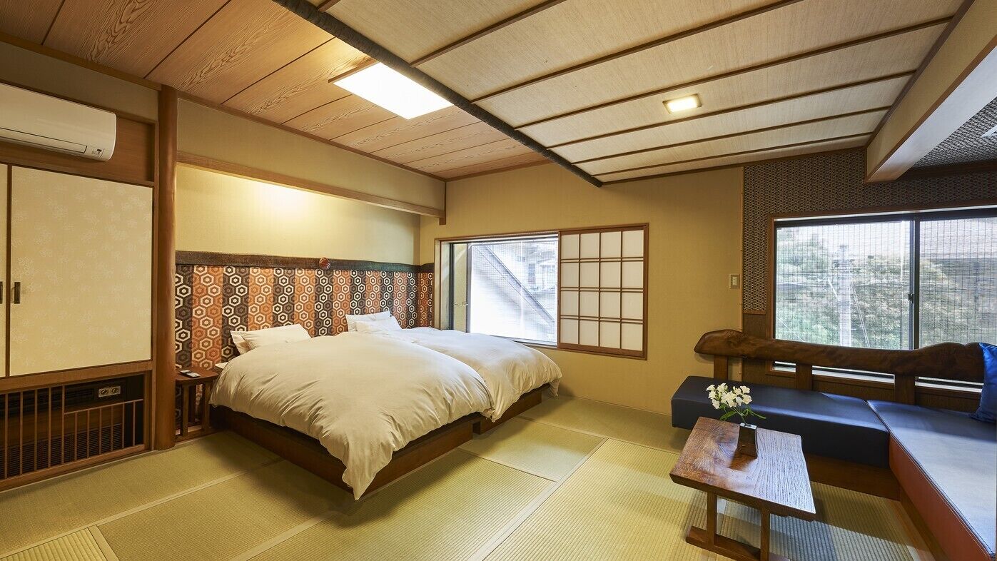 A traditional Japanese room with tatami flooring, a low bed, a sofa, and a sliding door.