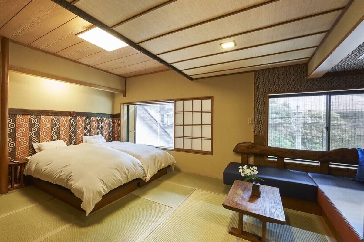 A traditional Japanese room with tatami flooring, a low bed, a sofa, and a sliding door.