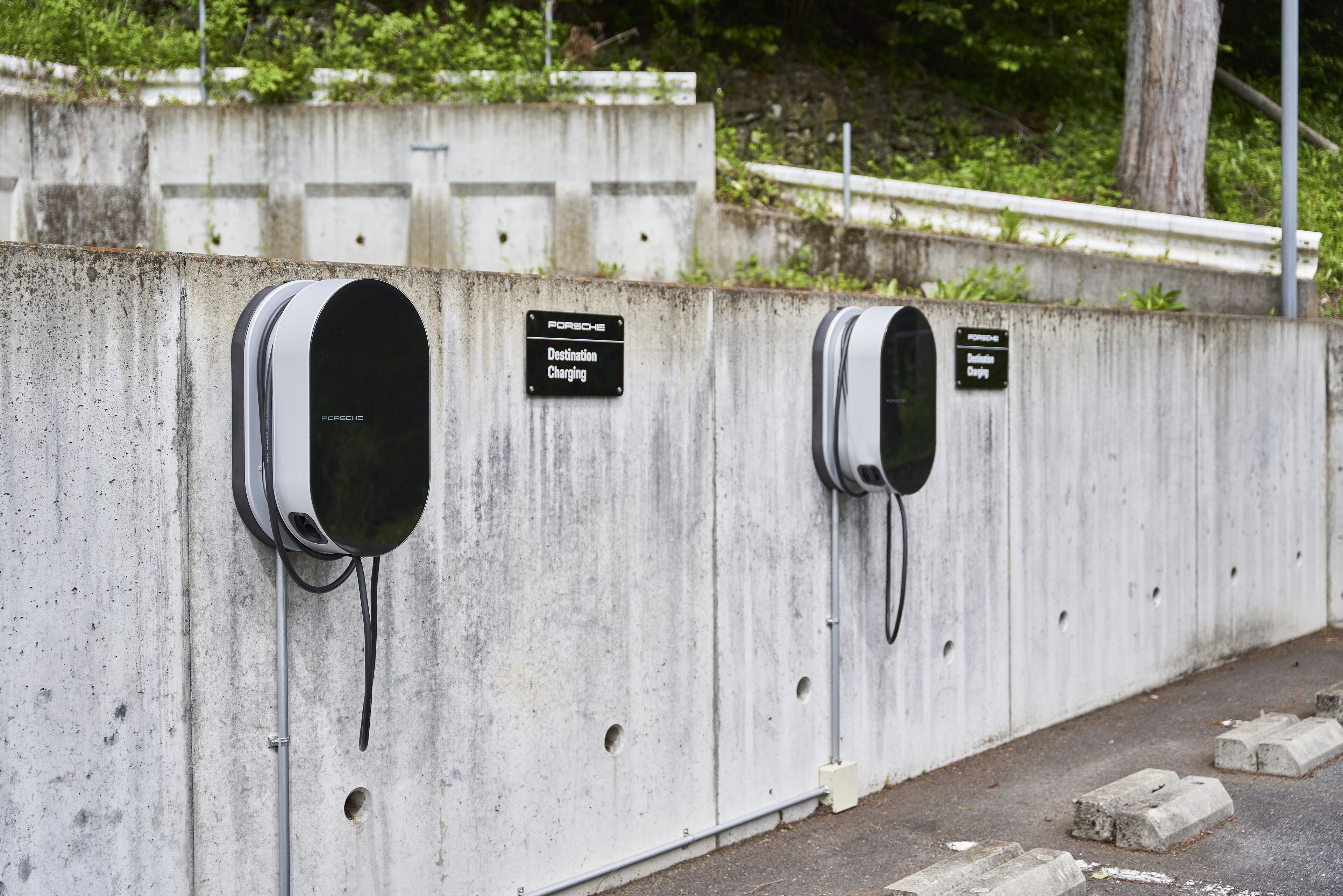Two electric vehicle charging stations mounted on a concrete wall with signs indicating 'Destination Charging' and 'Porsche Charging'.