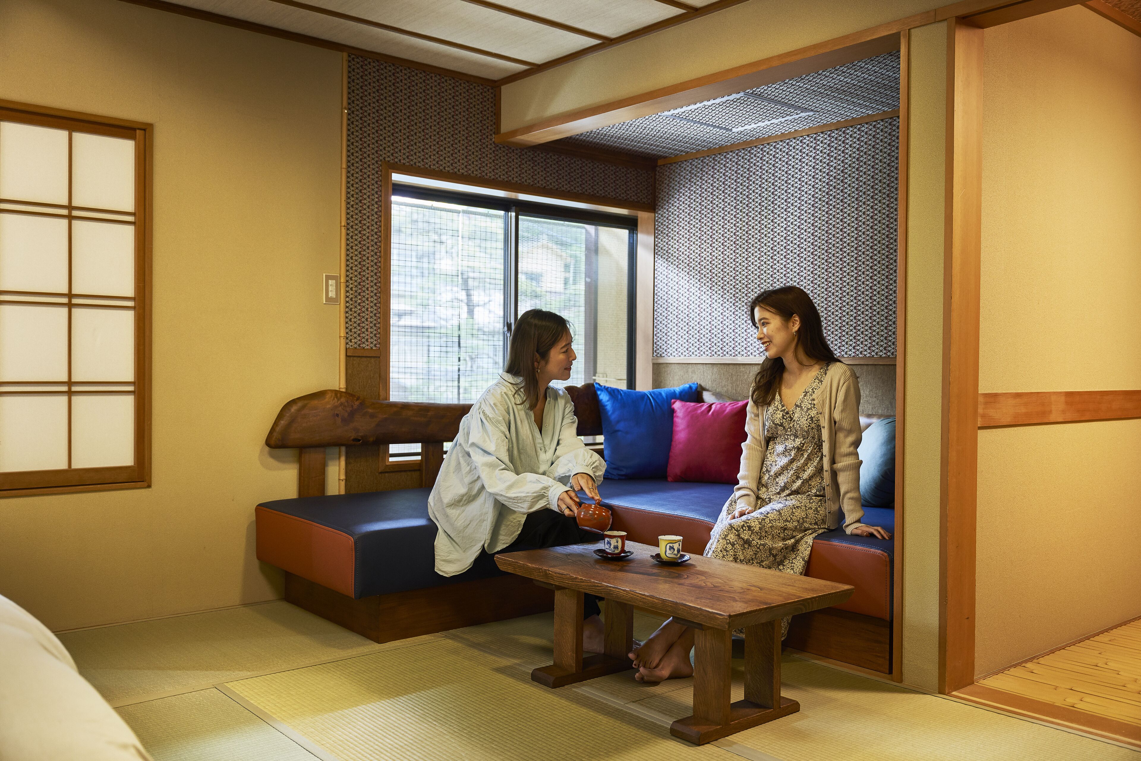 Ein traditioneller japanischer Raum mit Tatami-Boden, einem niedrigen Holztisch und einer Couch mit Kissen.