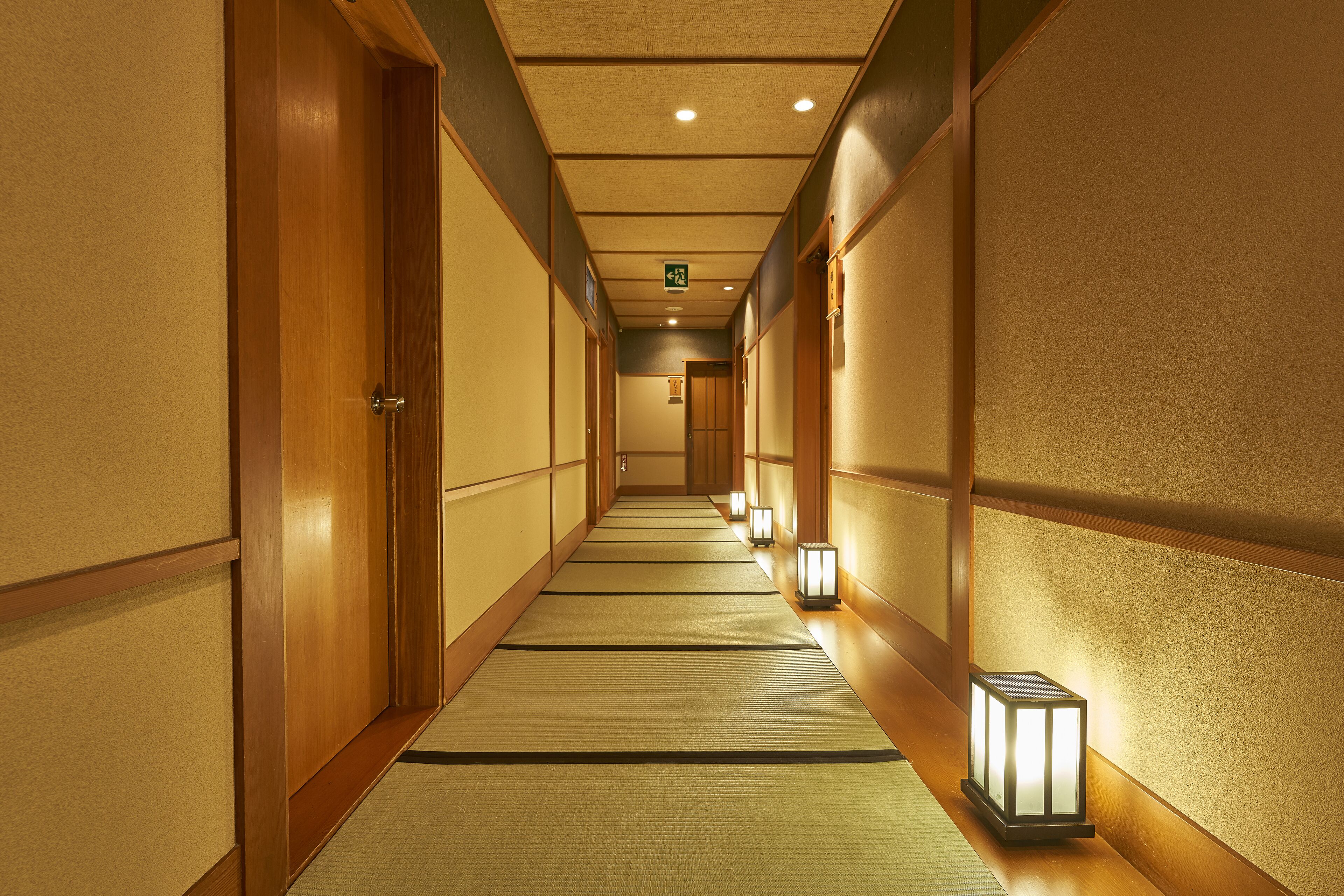 Un pasillo con esteras de tatami, puertas de madera y faroles tradicionales.