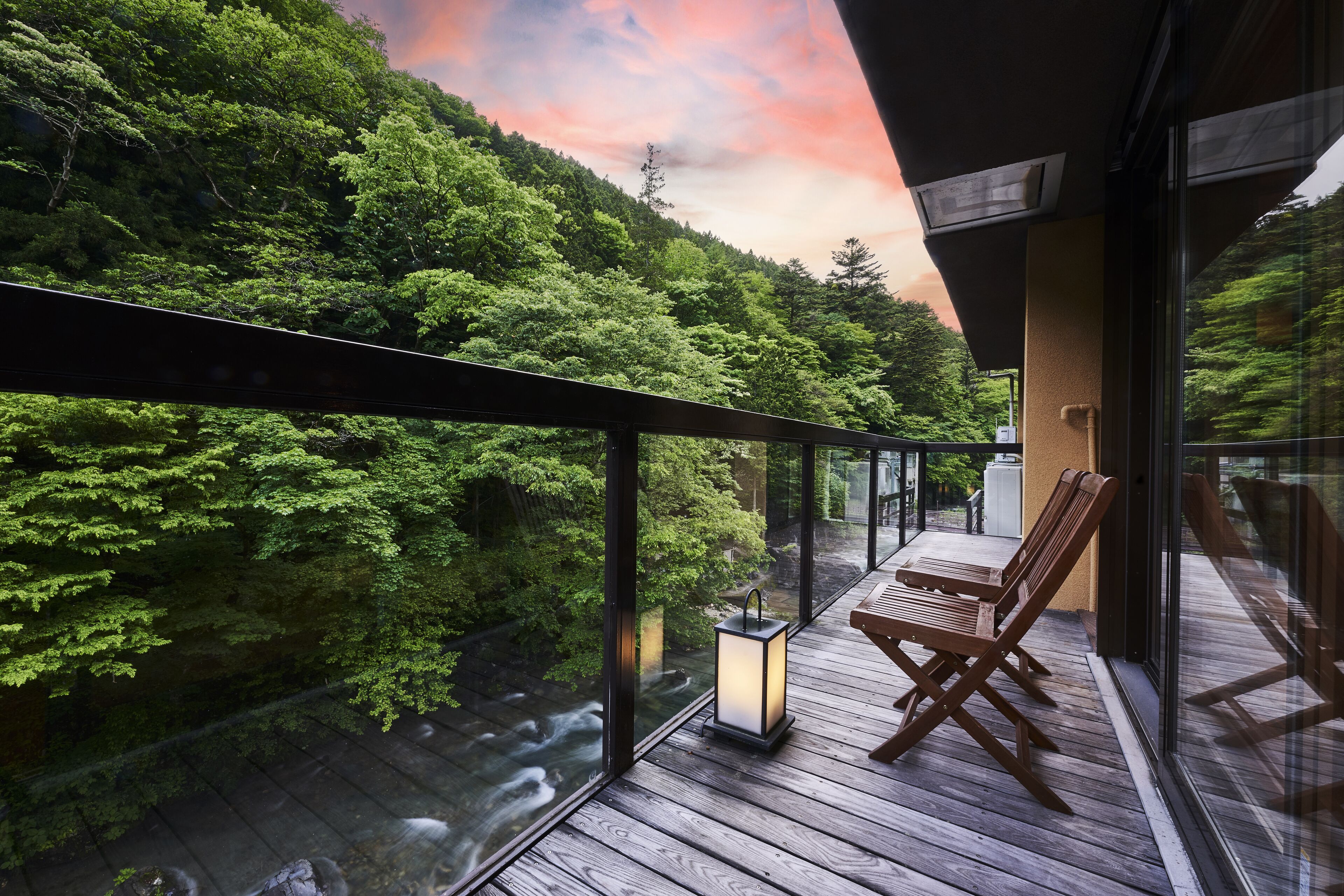 A balcony with wooden flooring, a table, and two chairs. A lantern is placed on the floor.