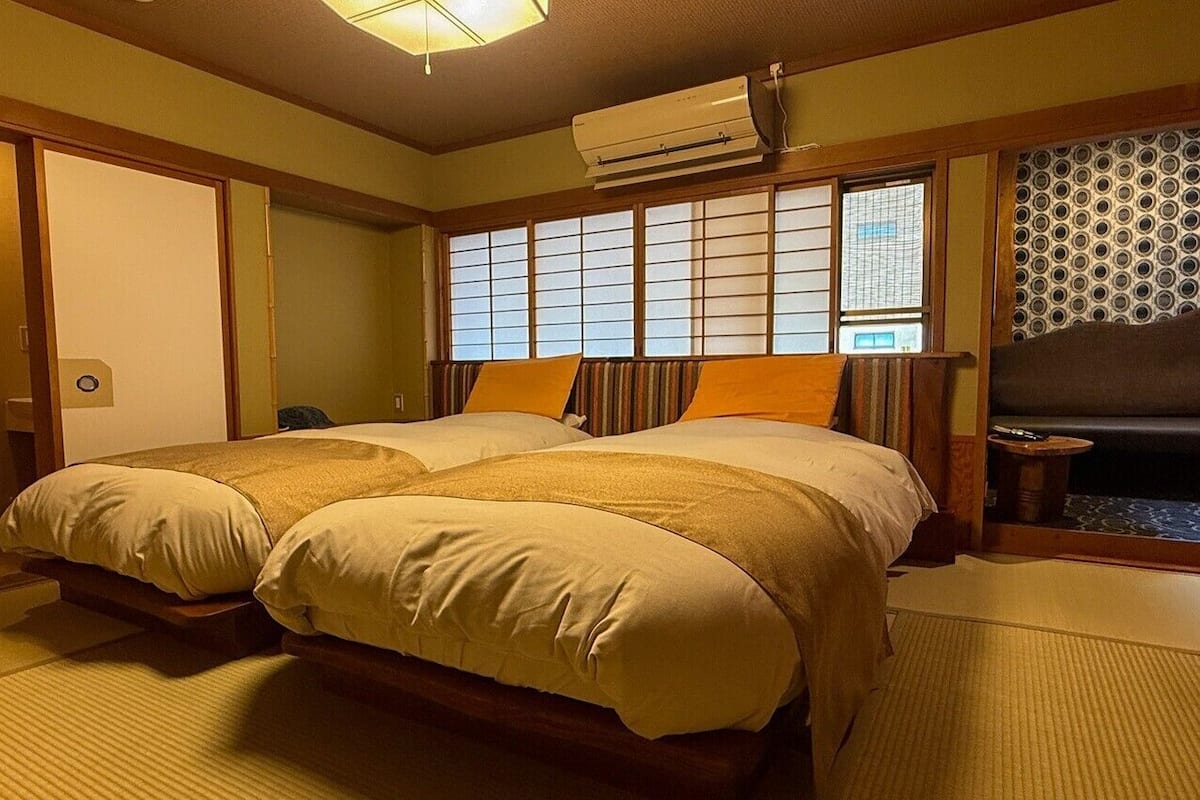 Una habitación tradicional japonesa con suelo de tatami, futón, puertas correderas y un separador shoji.