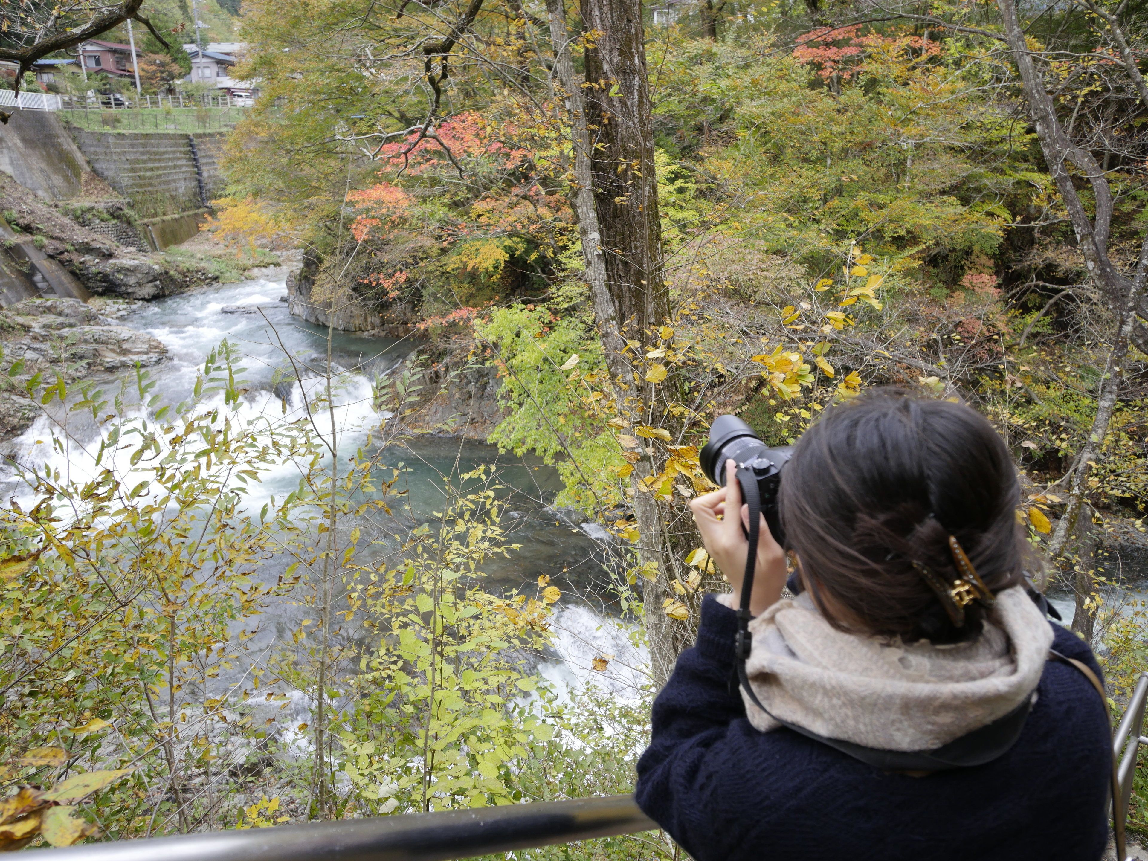 A person taking a photograph of a river with surrounding trees.