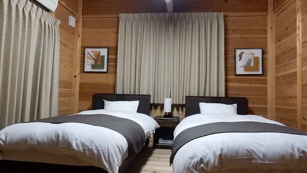 Habitación con dos camas, paredes de madera, ventilador de techo y ventana con cortinas.