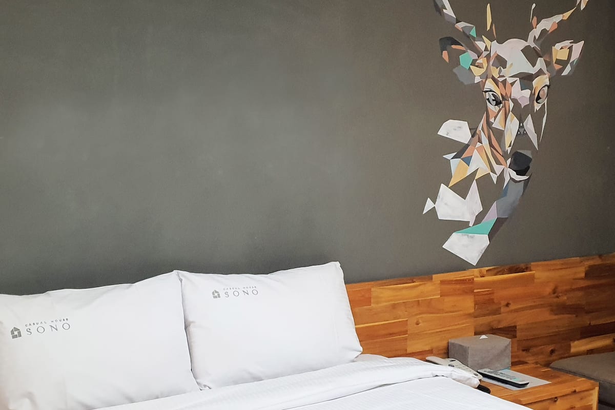 Ein Hotelzimmer mit Bett, weißen Kissen, einem Holzkopfteil und einem Wandbild.