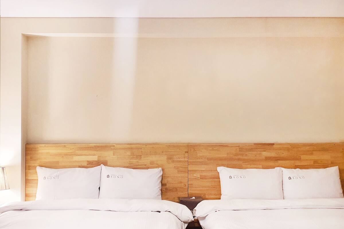 Ein Hotelzimmer mit einem Holzkopfteil, zwei weißen Betten mit passenden Kissen und einem Nachttisch.