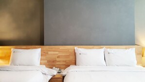 Een hotelkamer met twee bedden, elk met een wit kussen en een dekbed. Er is een houten hoofdbord, een nachtkastje met een telefoon, en een muur met een grijs paneel.