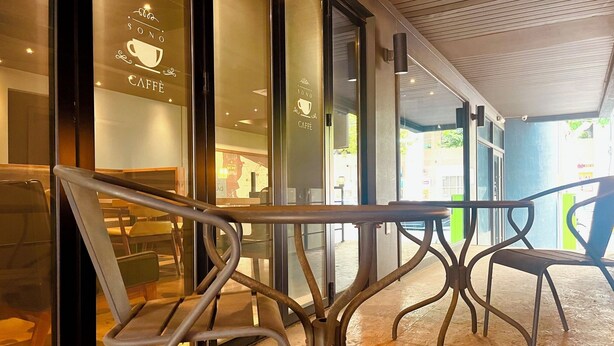 Een terras met metalen tafels en stoelen, glazen deuren en een houten plafond.