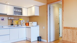 Een kleine keuken met witte kastjes, een magnetron en een spoelbak. Er staat een houten bankje en een deur naar een andere kamer.