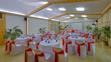 A conference room with multiple round tables, each with white tablecloths and red sashes, surrounded by chairs with white covers and red sashes.