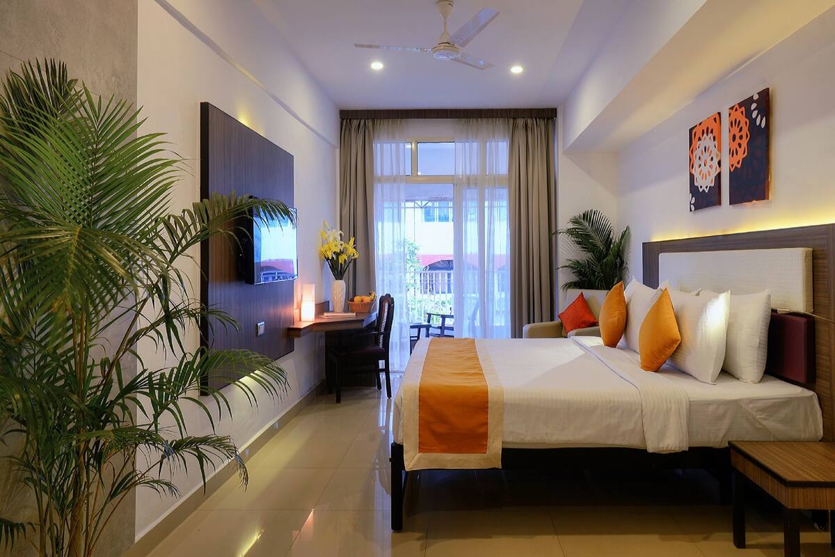 A hotel room with a bed, a desk, a TV, and a balcony with curtains.